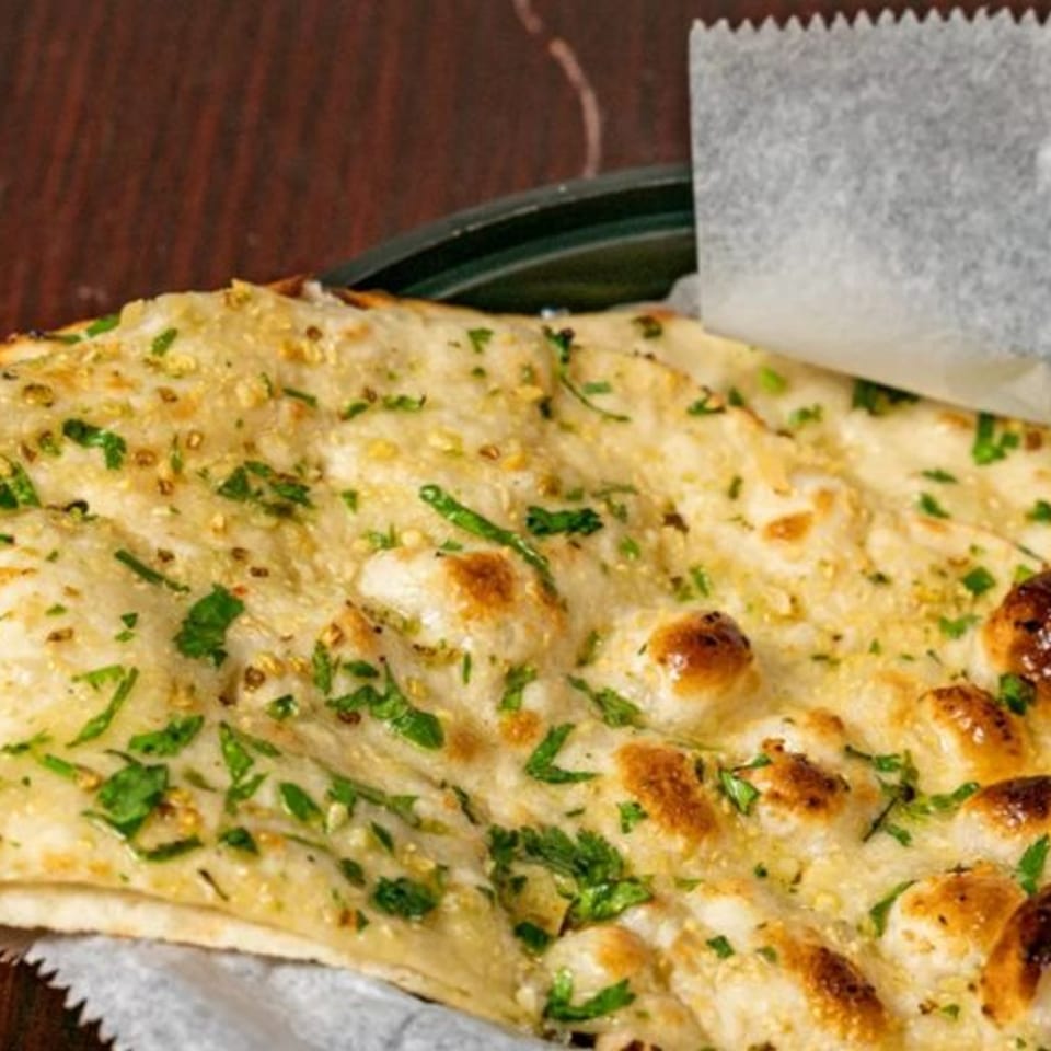 Close-up of garlic naan bread from Bombay Corner, garnished with fresh cilantro and sesame seeds.