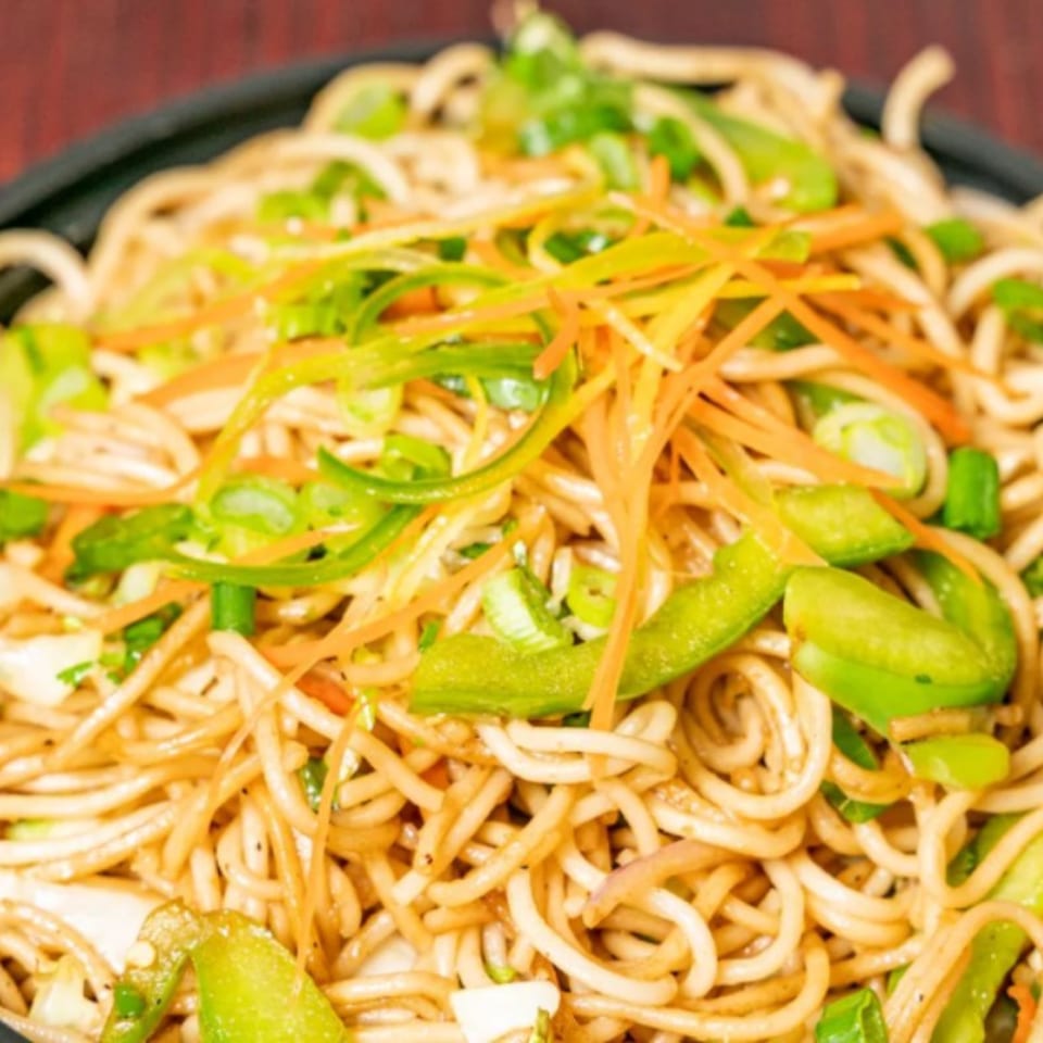 Close-up of Indian noodles with green bell peppers, carrots, and green onions.