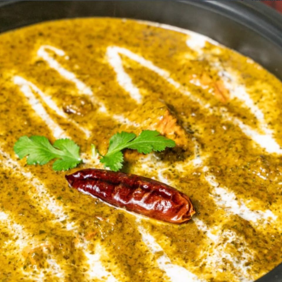 Bombay Corner's Indian curry, a vibrant green dish with white cream swirls, garnished with cilantro and a red chili.