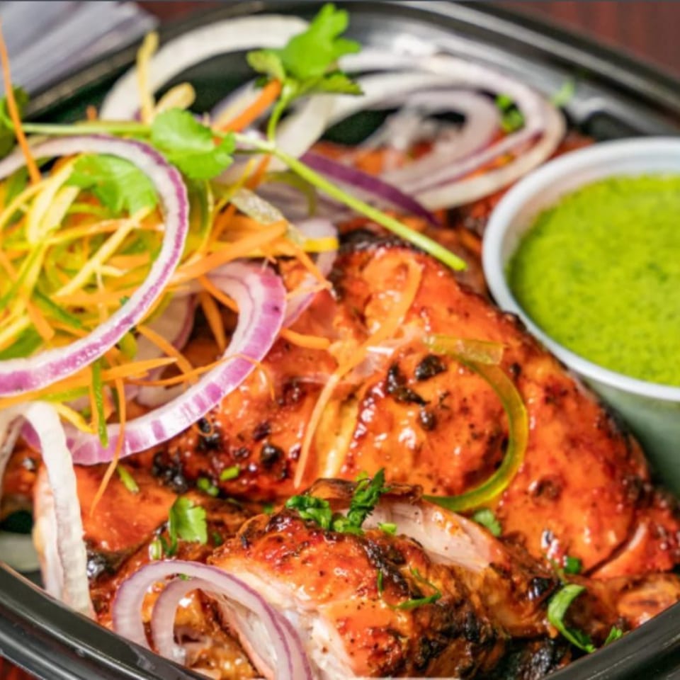 Bombay Corner's Tandoori Chicken, garnished with red onions and cilantro, served with green chutney.
